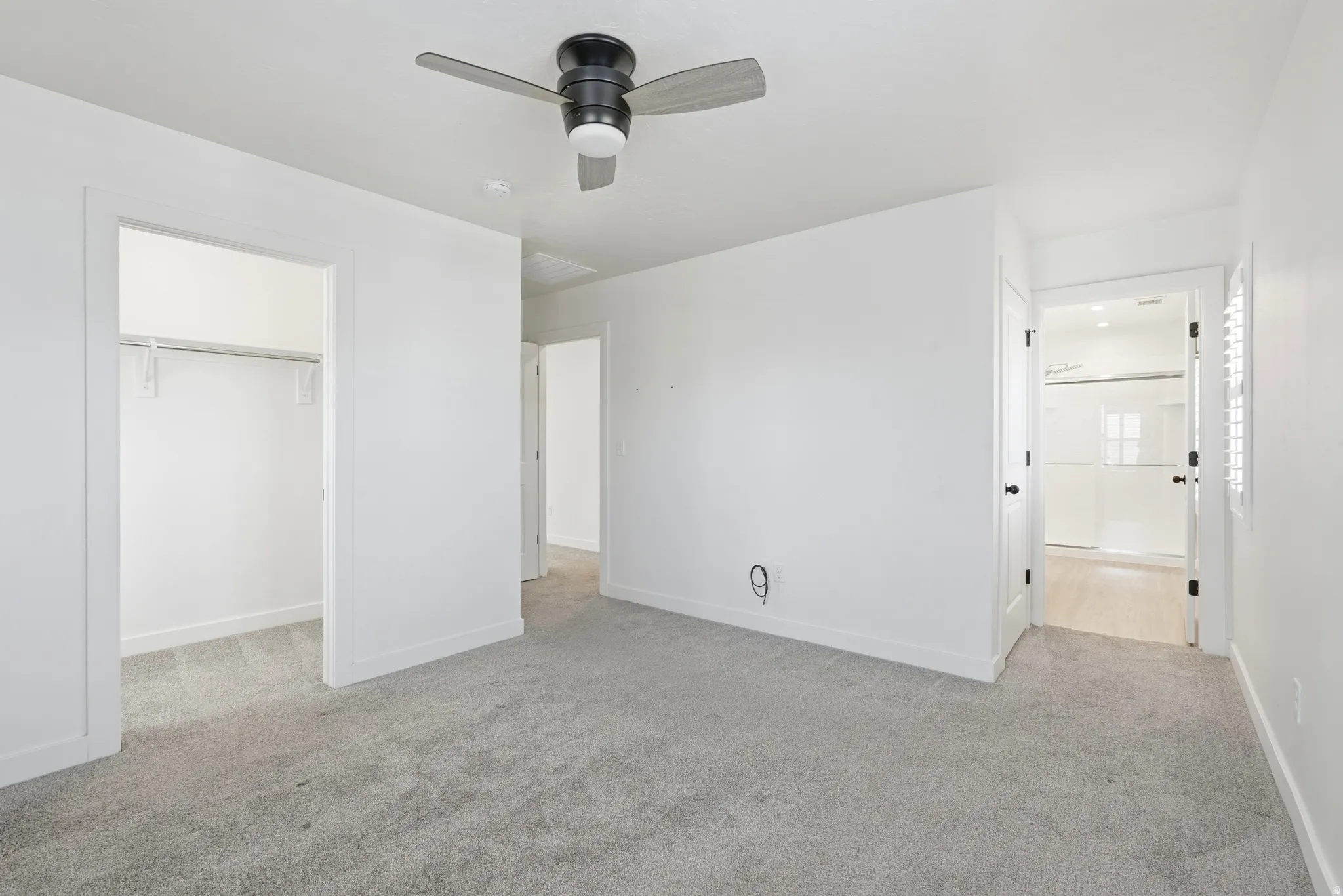 Spacious room featuring light grey carpet, a modern ceiling fan, and crisp white walls