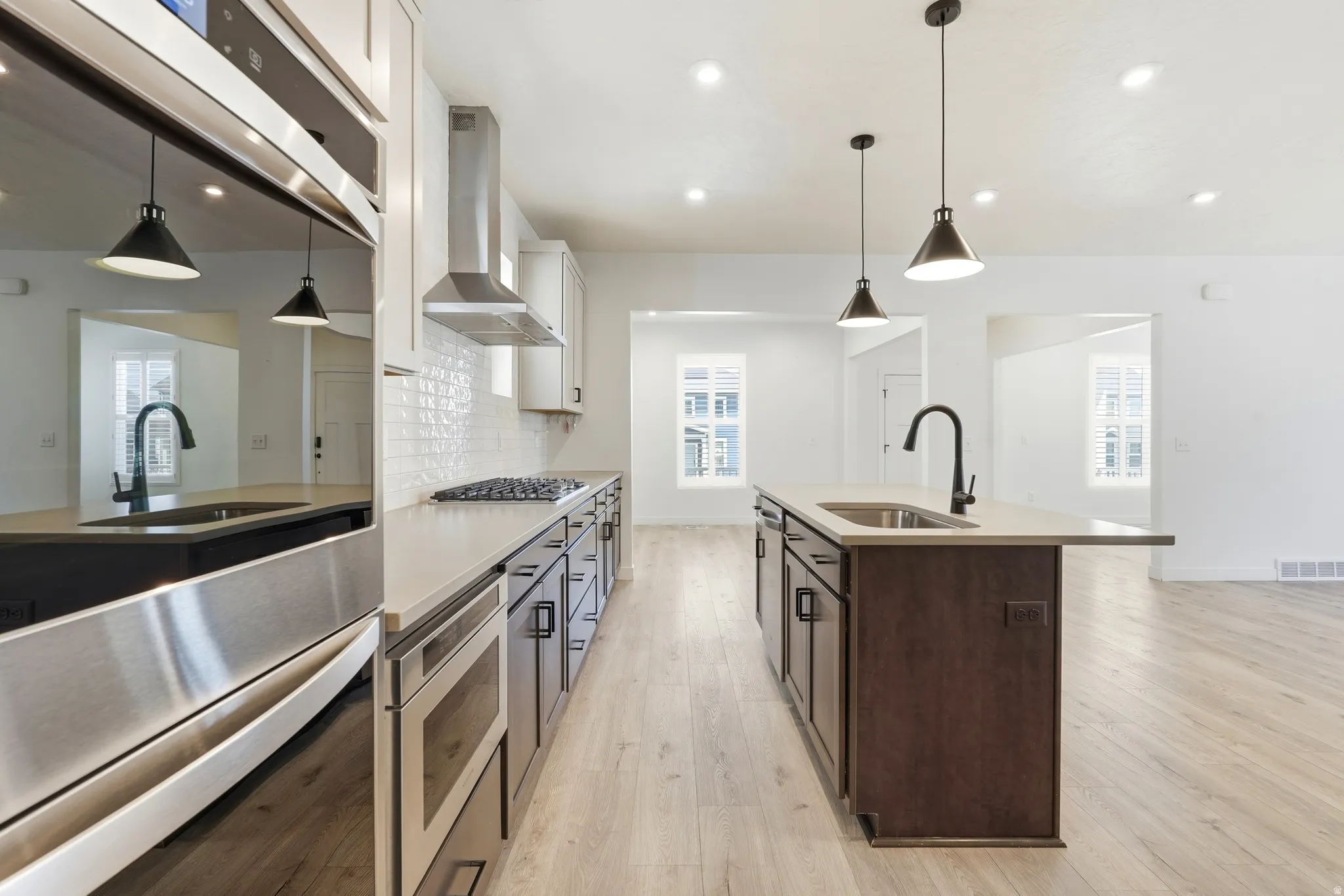 Modern kitchen featuring stainless steel appliances, light wood-finish flooring, recessed lighting, and an island with a built-in sink and pendant lights