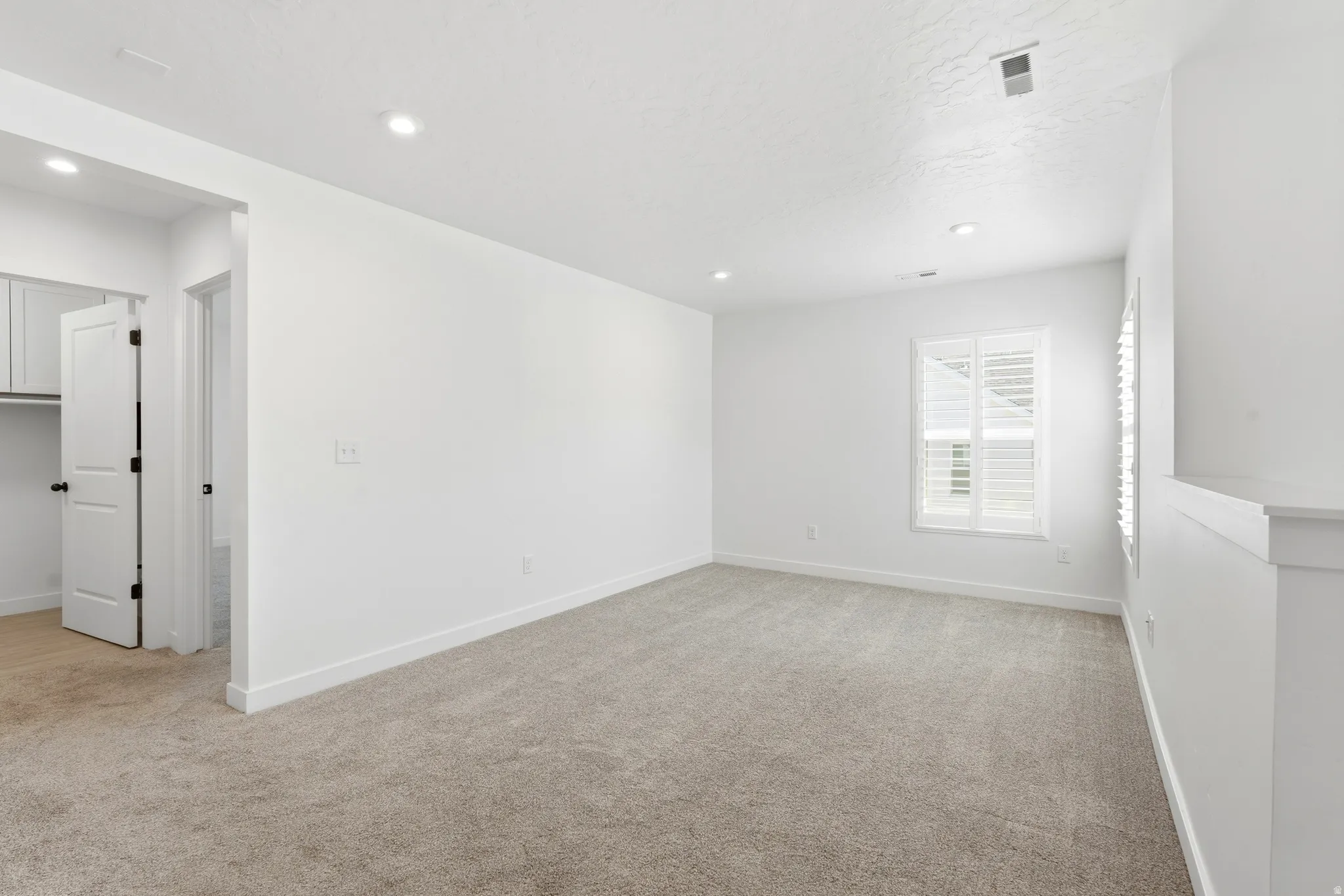 Carpeted room with recessed lighting and a window featuring white plantation shutters
