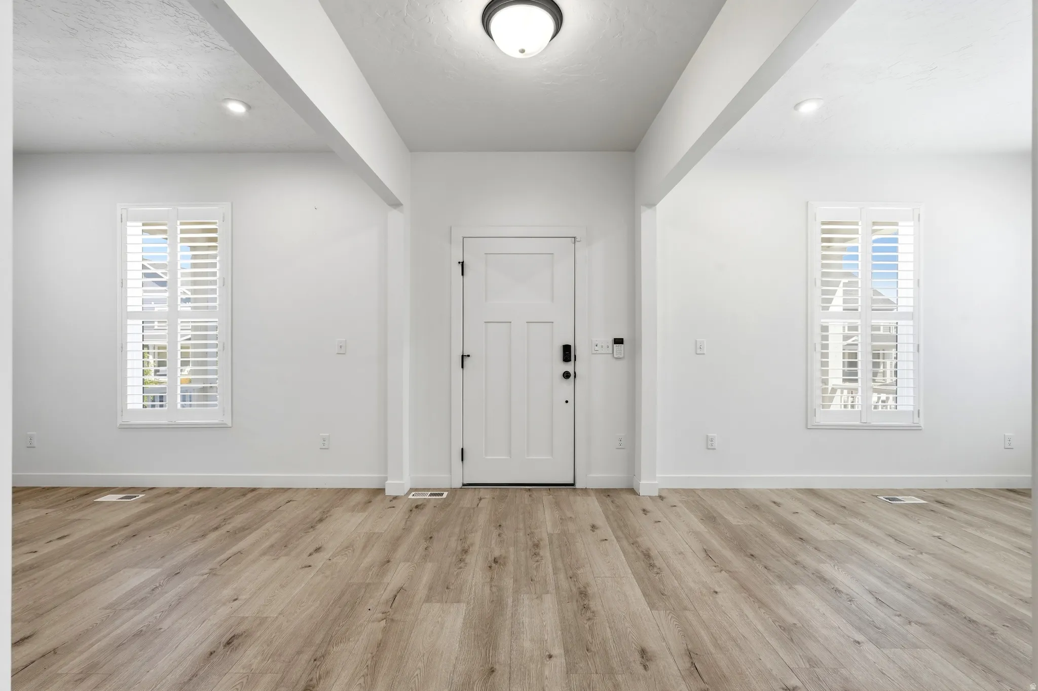 Entryway featuring a panel door with smart lock technology, wood-finish flooring, two large windows with plantation shutters, recessed ceiling lighting, and a flush mount fixture