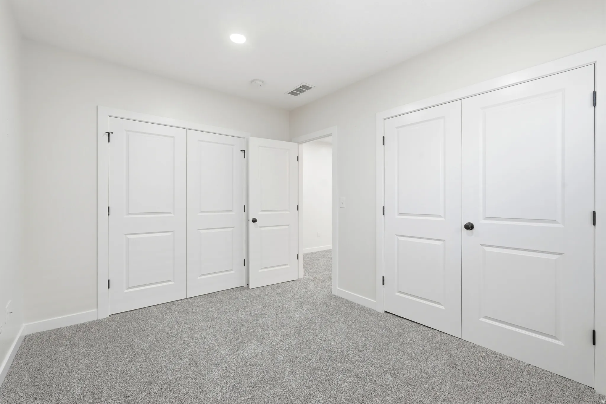 Room featuring light gray carpeting, crisp white walls, and bright recessed lighting