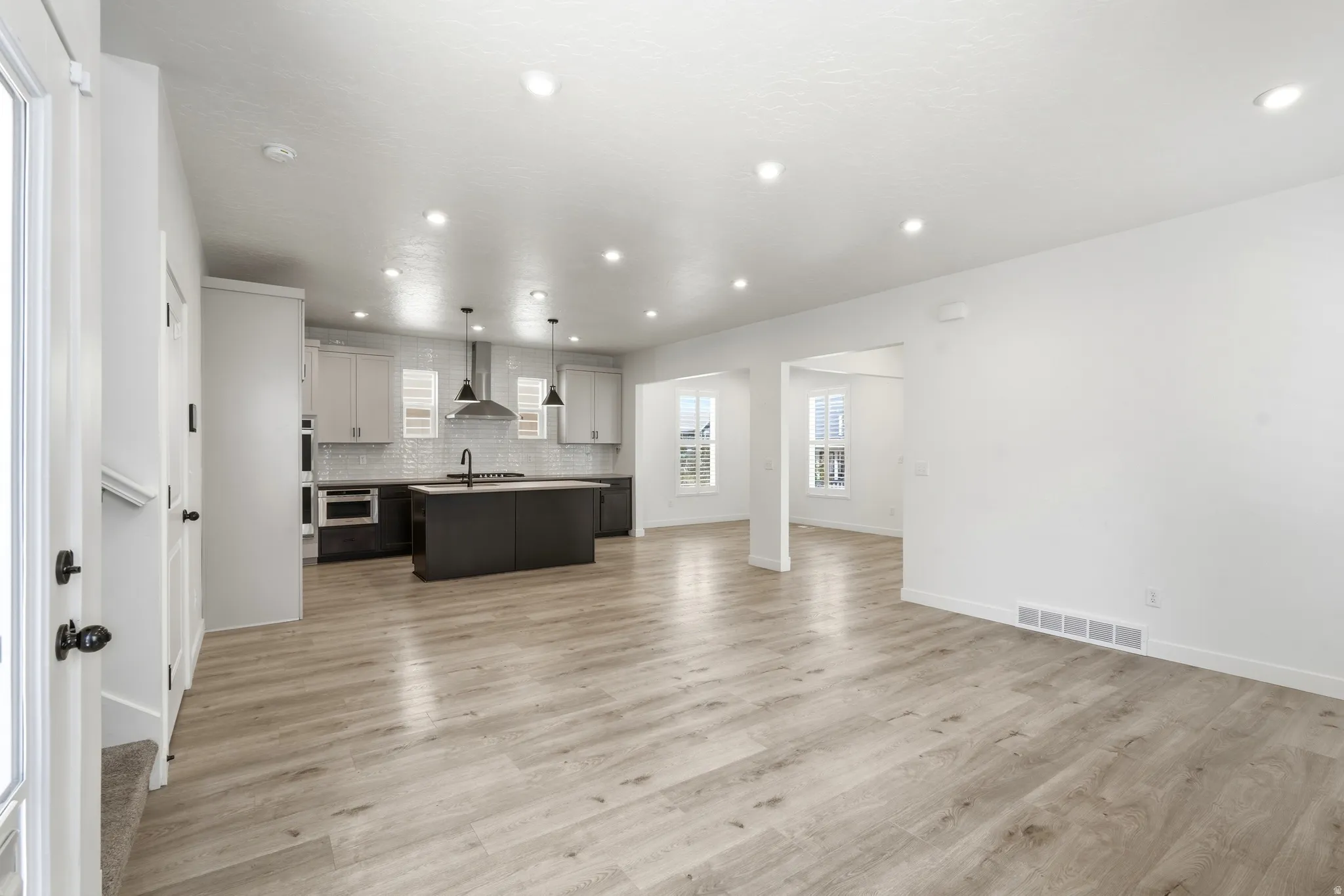 Open-concept living space featuring wood-finish flooring, recessed lighting, and a modern kitchen with a large island and stainless steel appliances