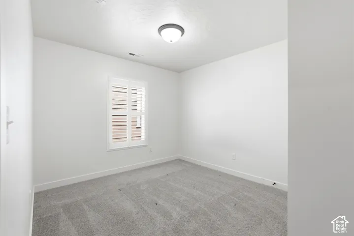 Bright room featuring white walls, gray carpet, a single window with white plantation shutters, and a flush-mount ceiling light fixture