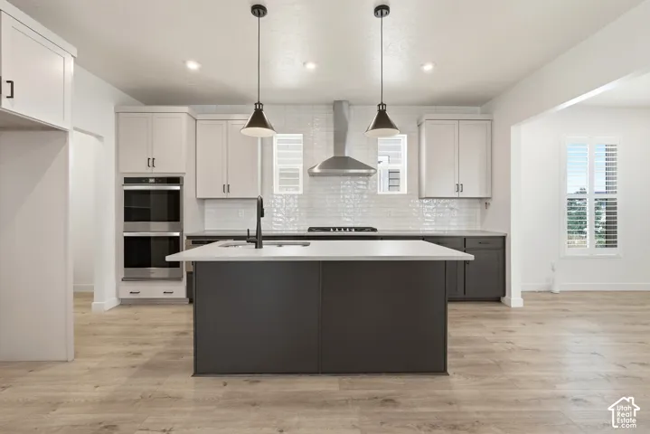 Contemporary kitchen featuring a large central island with a sink, light wood-finish flooring, white upper cabinetry, dark lower cabinetry, and a subway tile backsplash
