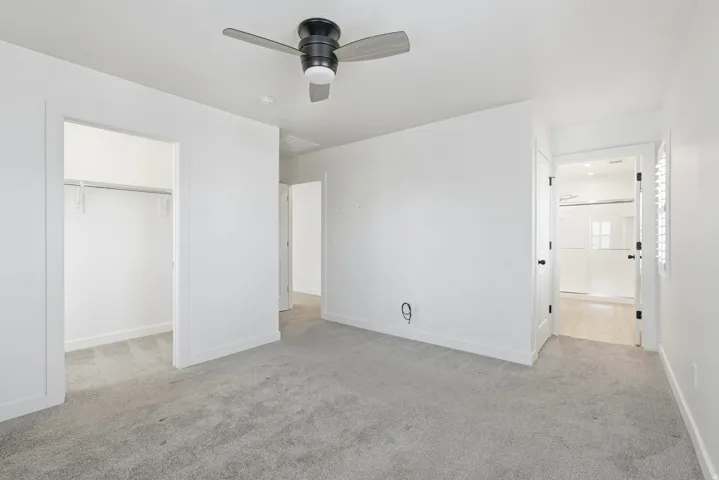 Spacious room featuring light grey carpet, a modern ceiling fan, and crisp white walls