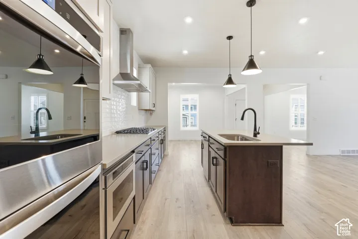 Modern kitchen featuring stainless steel appliances, light wood-finish flooring, recessed lighting, and an island with a built-in sink and pendant lights