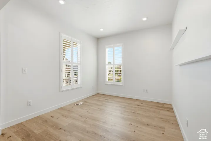 Bright room featuring two windows with plantation shutters, recessed lighting, wood-finish flooring, and built-in wall shelving