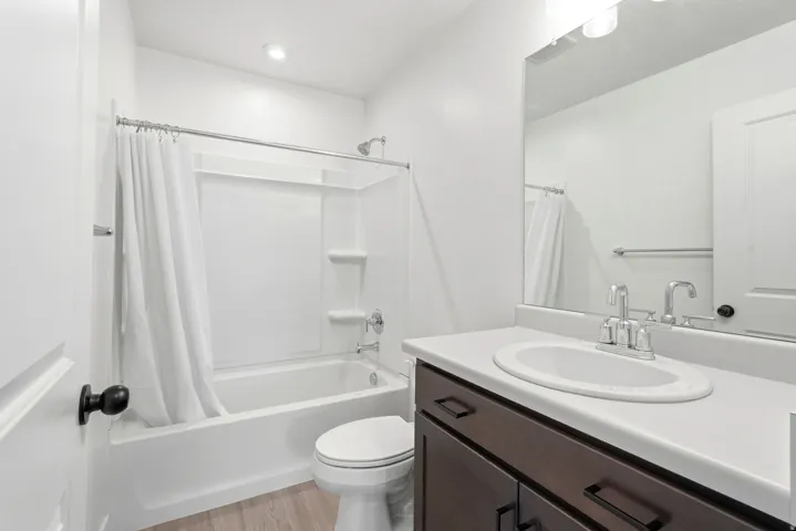 Bathroom featuring a white tub/shower combination, dark wood-finish vanity with a light-colored countertop, and a large wall-mounted mirror