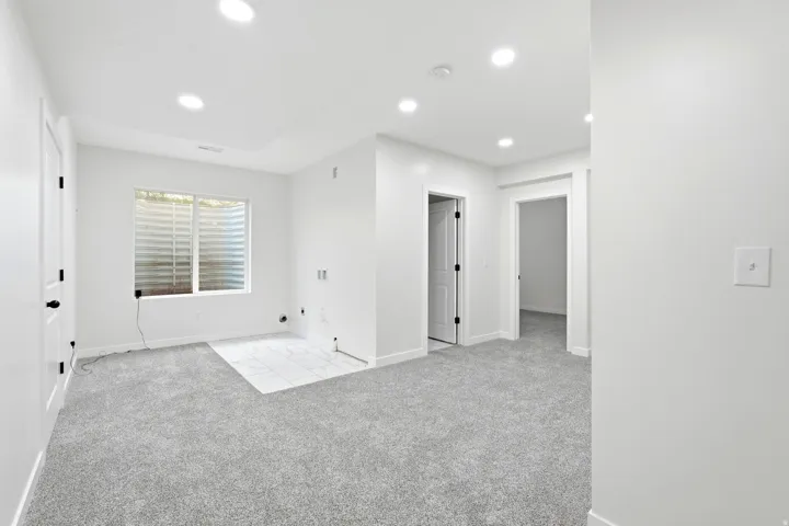 Spacious interior featuring light gray carpeting, a window with horizontal blinds, and recessed lighting