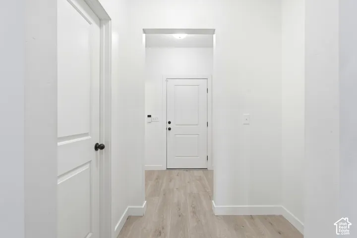 Hallway with light wood-finish flooring, white baseboards, and white walls