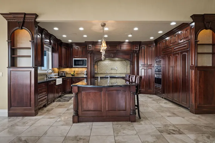 Kitchen featuring an island with sink, dark stone countertops, a breakfast bar, built in appliances, and hanging light fixtures