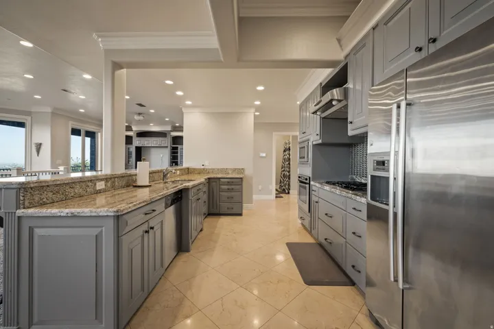 Two tone kitchen with stainless steel appliances, light stone counters, ornamental molding, recessed lighting, and backsplash