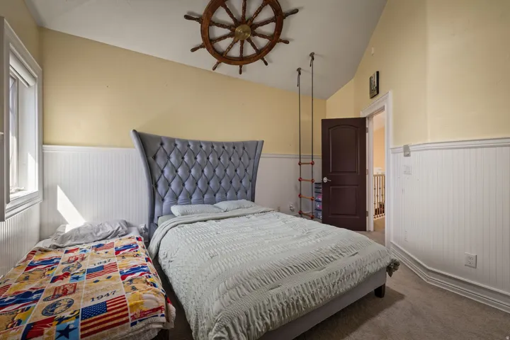 Carpeted bedroom featuring a wainscoted wall and vaulted ceiling