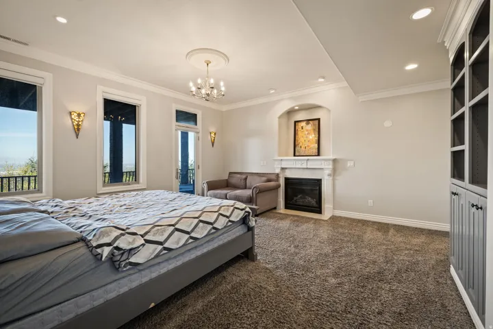 Bedroom featuring crown molding, dark carpet, a fireplace with flush hearth, a chandelier, and access to outside