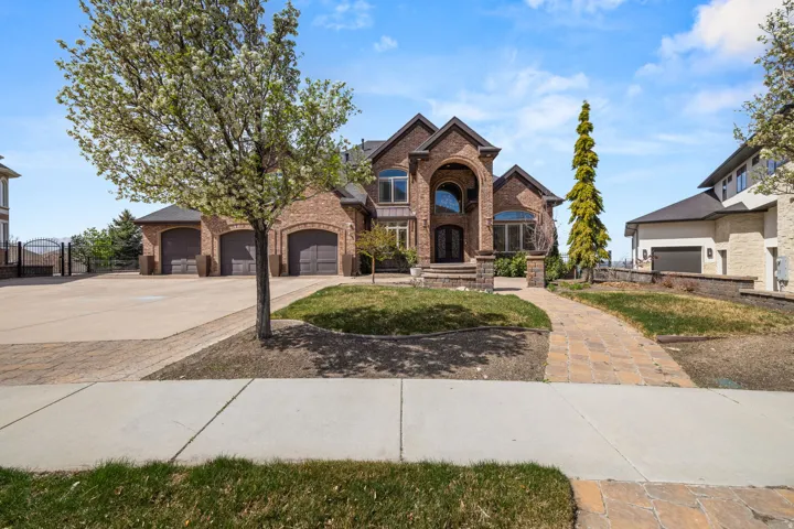 French country inspired facade with brick siding, driveway, a gate, and an attached garage