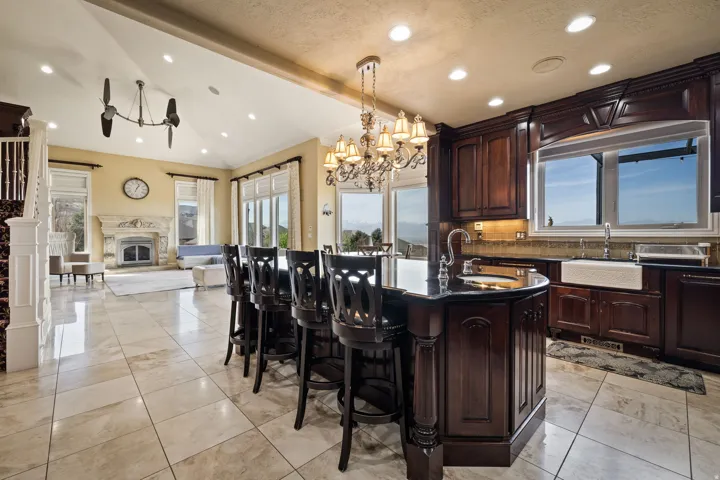 Kitchen featuring backsplash, a center island with sink, suspended lighting, open floor plan, and dark stone counters
