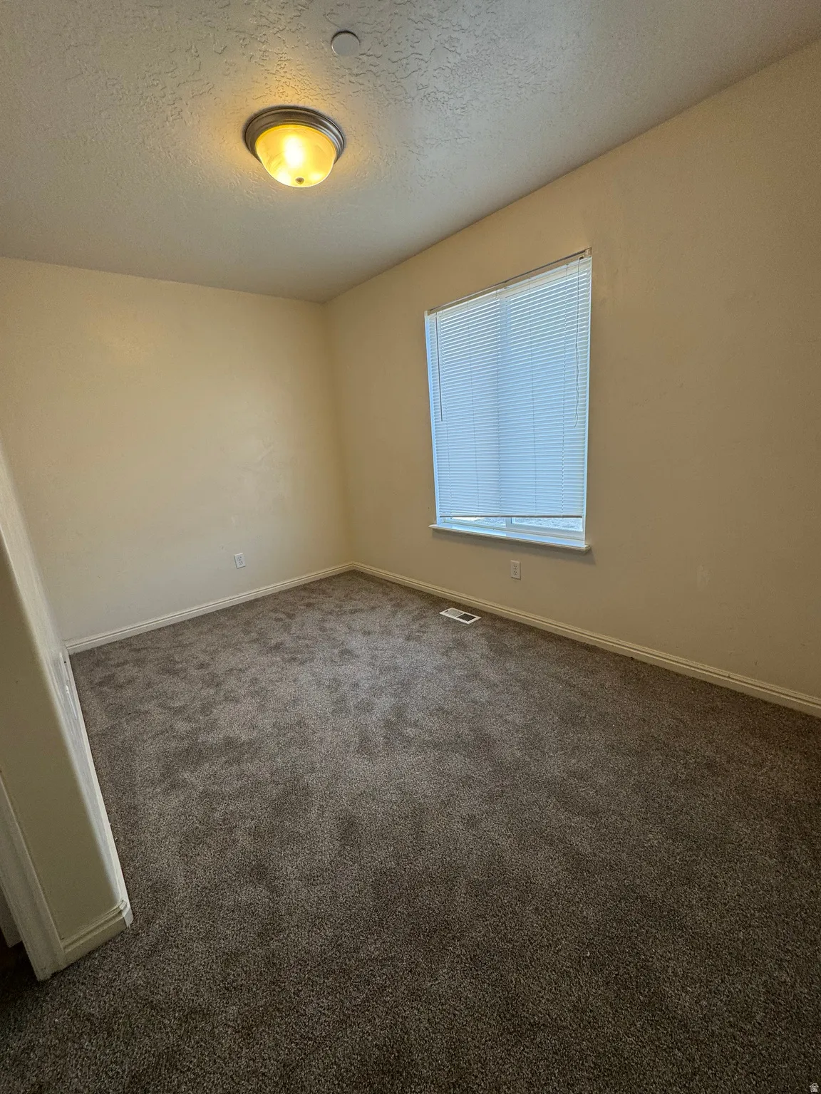 Empty room featuring a textured ceiling and dark carpet