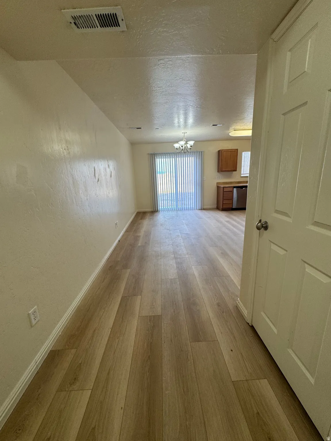 Unfurnished living room featuring a textured ceiling, light wood-type flooring, a textured wall, and a chandelier