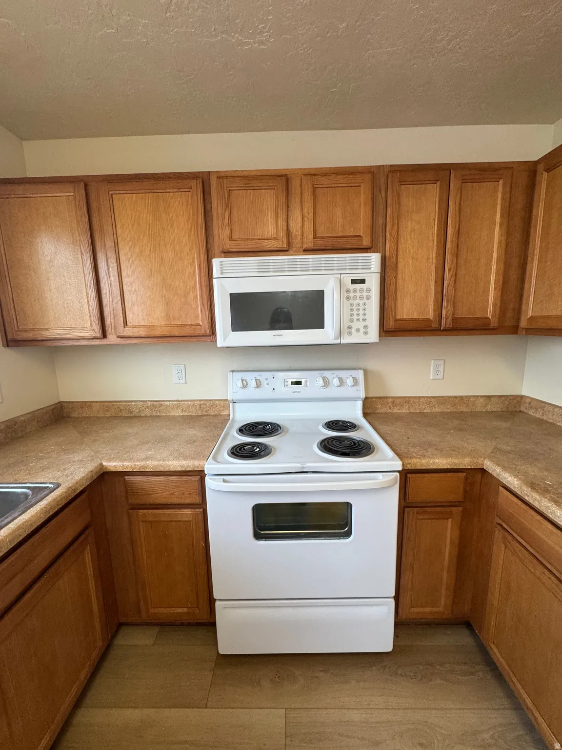 Kitchen with white appliances, light countertops, a textured ceiling, wood finish cabinets, and light wood-style flooring