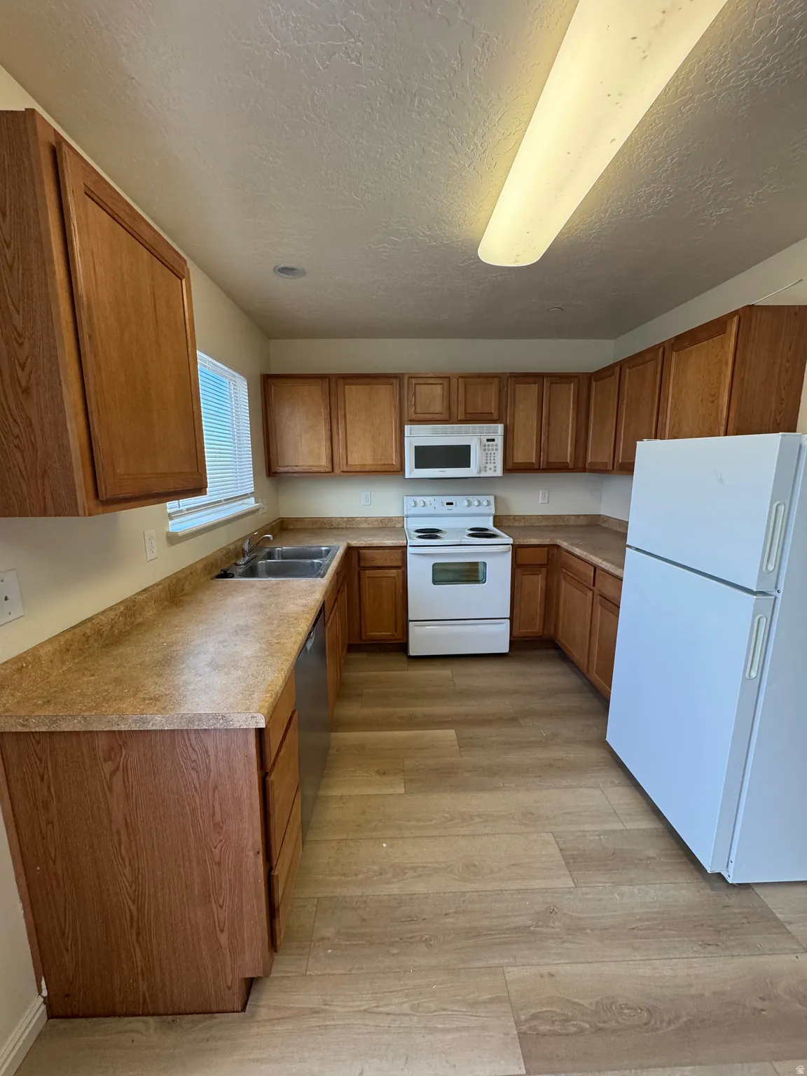 Kitchen with white appliances, wood finish cabinets, light countertops, light wood-style flooring, and a textured ceiling
