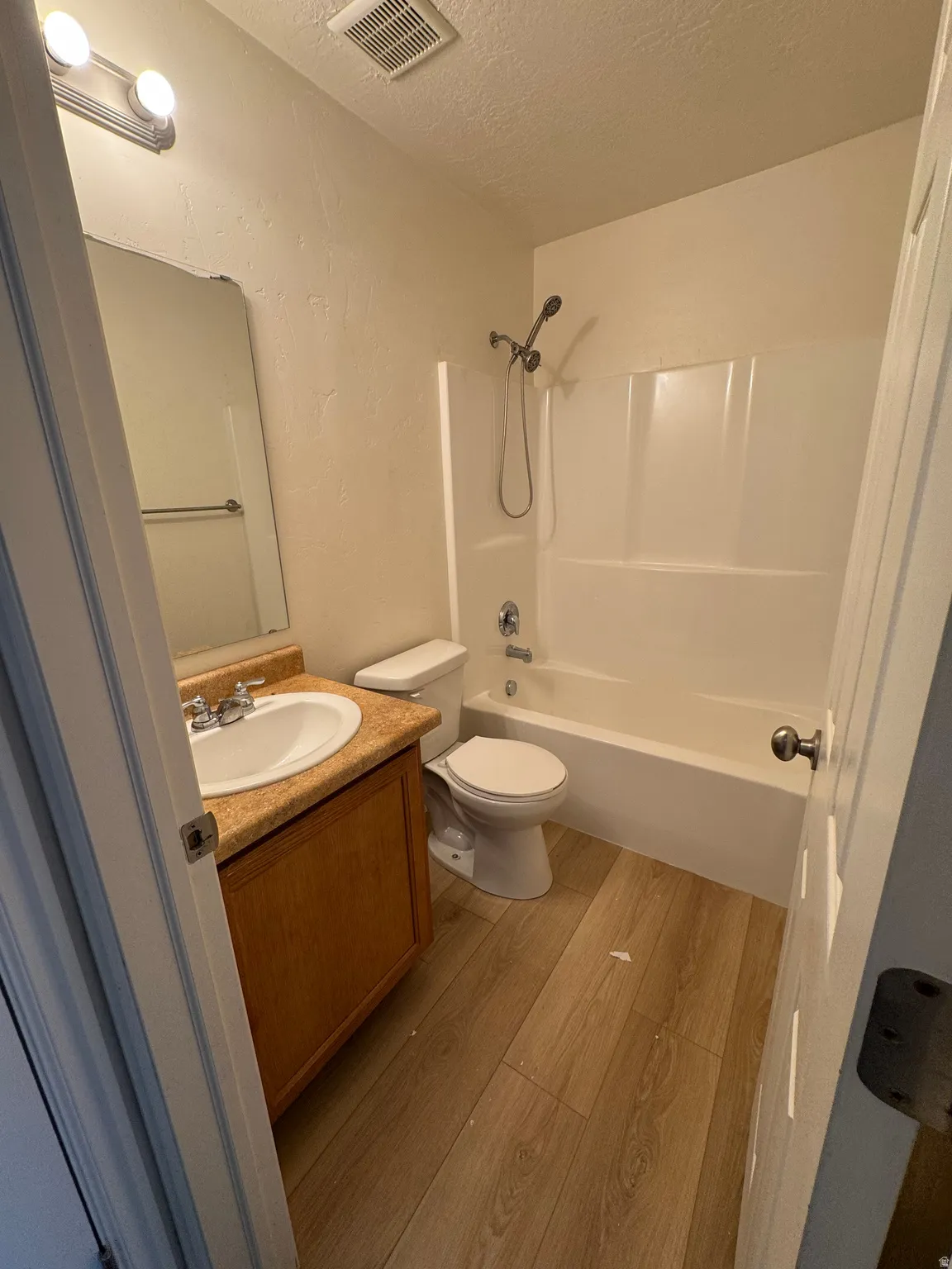 Bathroom with a textured ceiling, vanity, light wood-style floors, tub / shower combination, and a textured wall