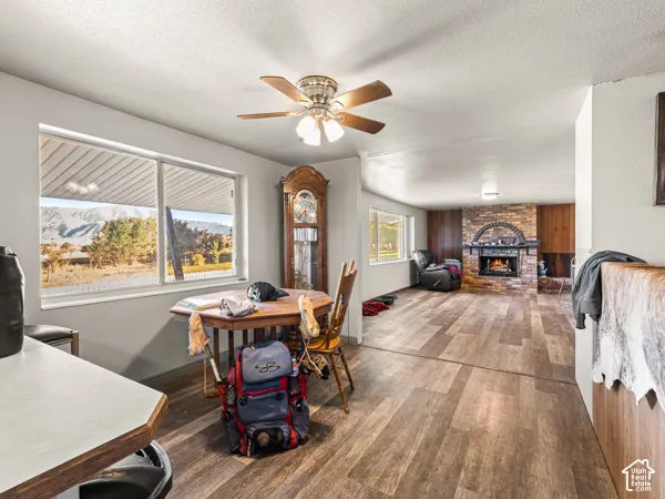 Dining room with dark wood-style floors, a fireplace, a ceiling fan, and a textured ceiling