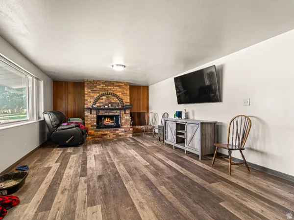Living area featuring a brick fireplace, dark wood-style floors, wood walls, and a textured ceiling