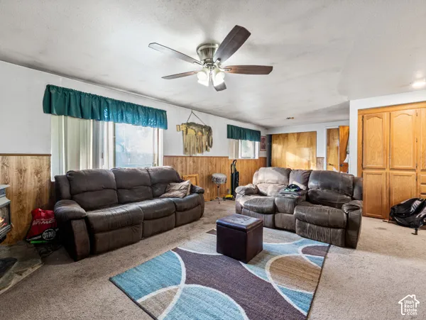 Carpeted living area with wood walls, wainscoting, a ceiling fan, a wood stove, and a textured ceiling