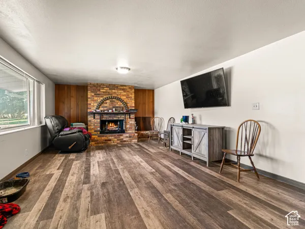 Living area featuring a brick fireplace, dark wood-style floors, wood walls, and a textured ceiling