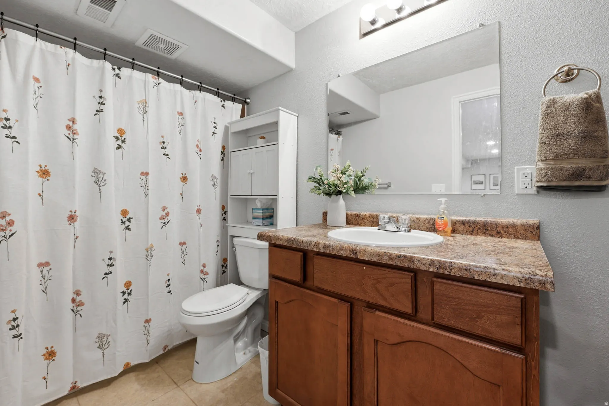 Bathroom featuring vanity, curtained shower, a textured wall, and light tile patterned floors