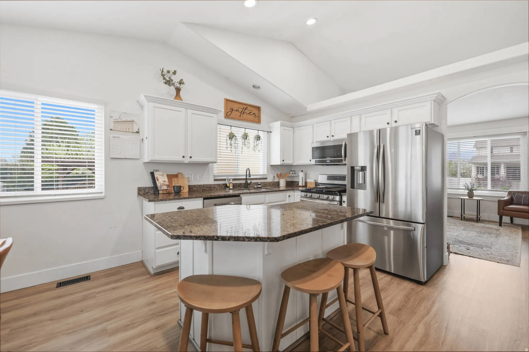 Kitchen with stainless steel appliances, white cabinetry, a kitchen bar, dark stone counters, and lofted ceiling