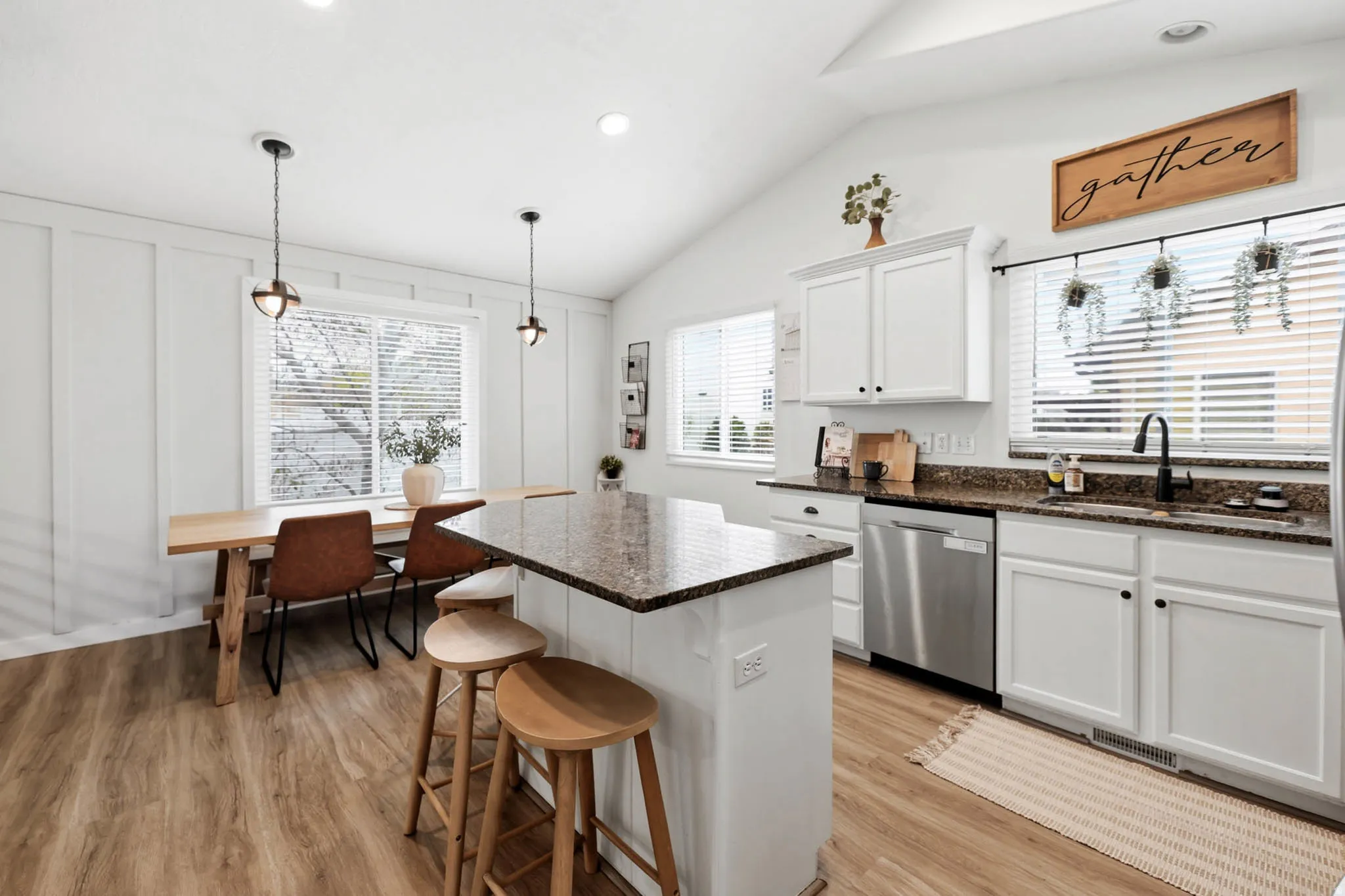 Kitchen with white cabinets, a kitchen breakfast bar, light wood-type flooring, dark stone countertops, and lofted ceiling