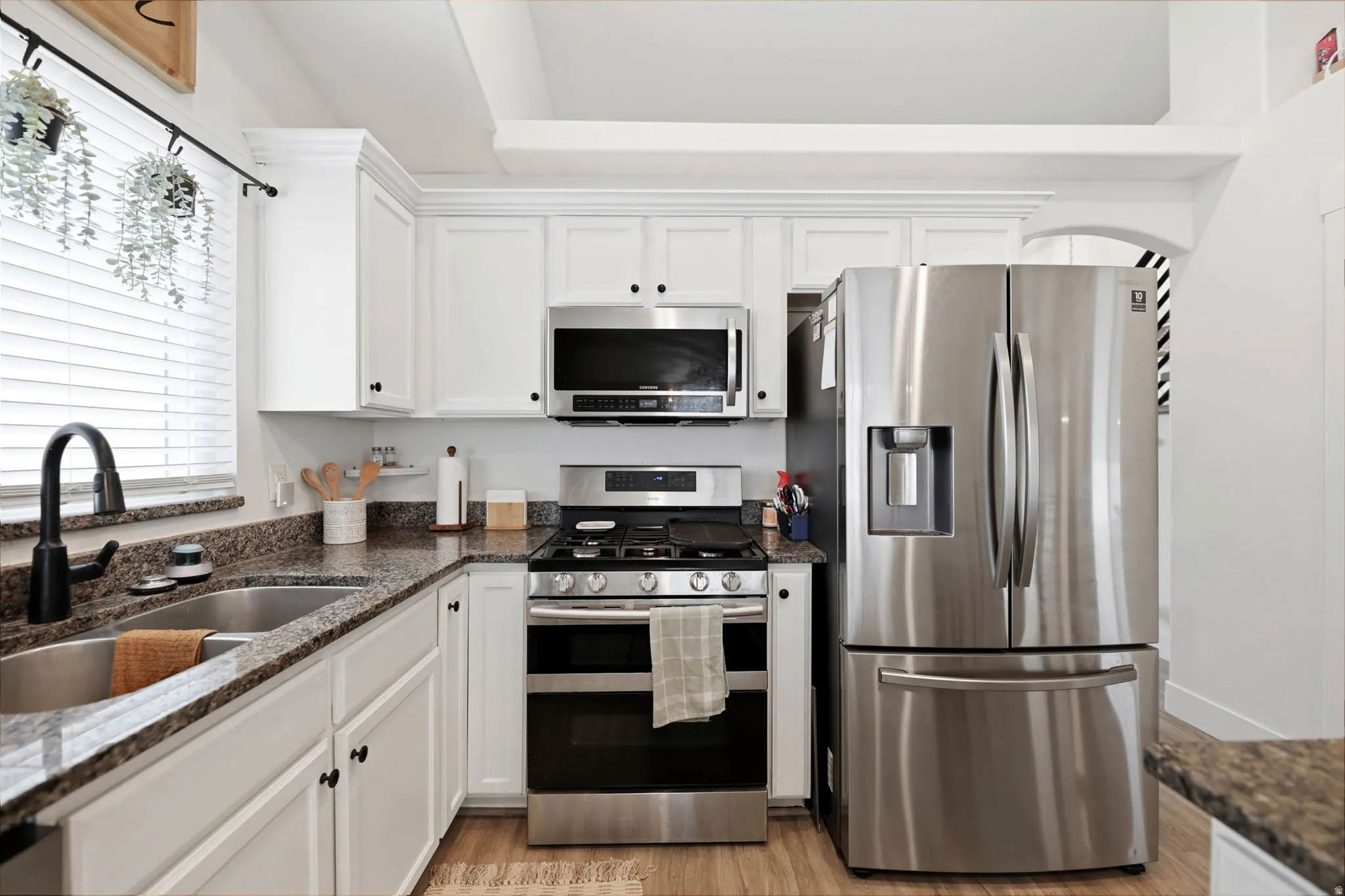 Kitchen featuring stainless steel appliances, white cabinetry, and dark stone countertops