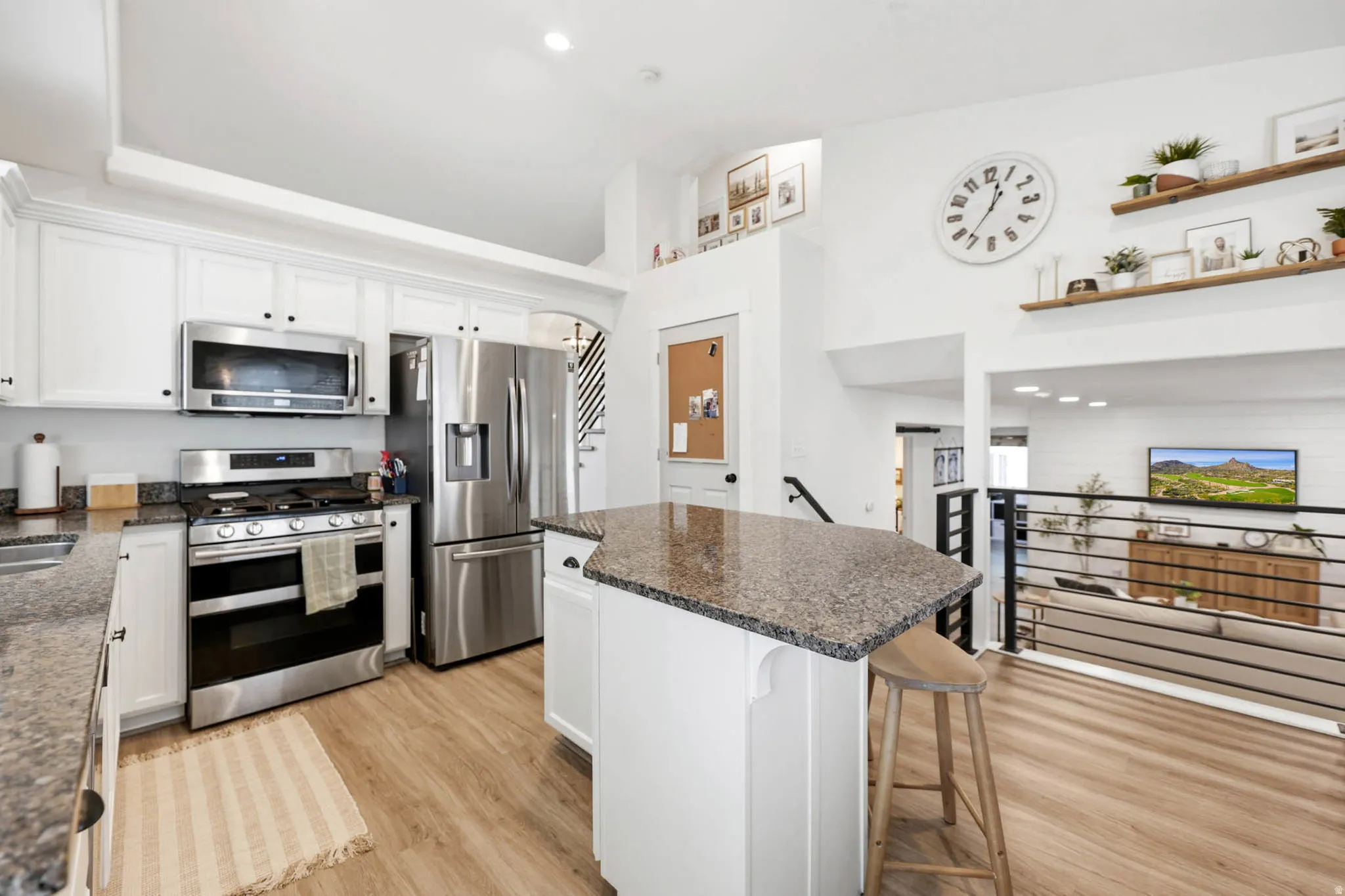 Kitchen with stainless steel appliances, a kitchen island, white cabinetry, light wood finished floors, and vaulted ceiling