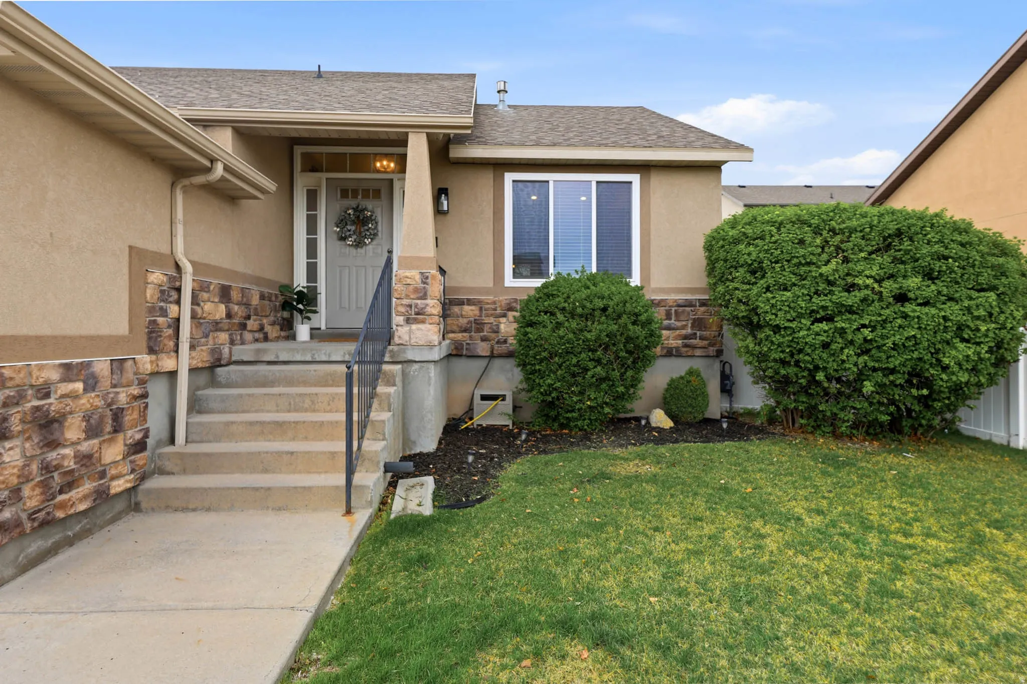 Entrance to property featuring stone siding, stucco siding, a yard, and roof with shingles
