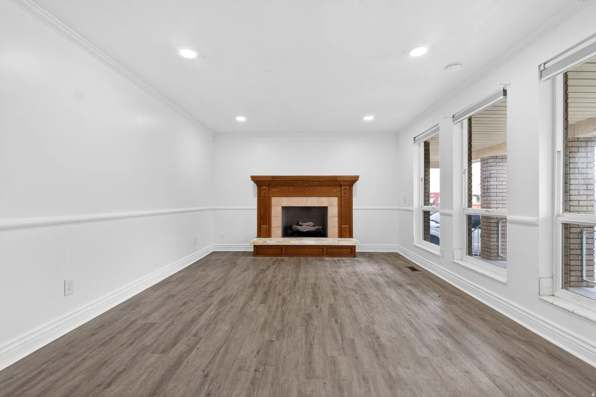 Unfurnished living room with a tiled fireplace, dark wood finished floors, recessed lighting, and crown molding
