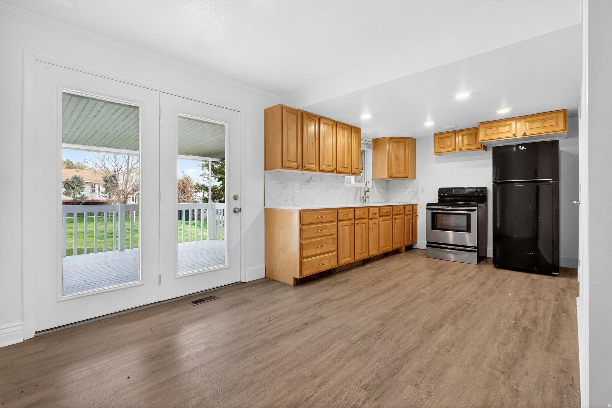 Kitchen with freestanding refrigerator, light countertops, stainless steel electric stove, dark wood-type flooring, and crown molding