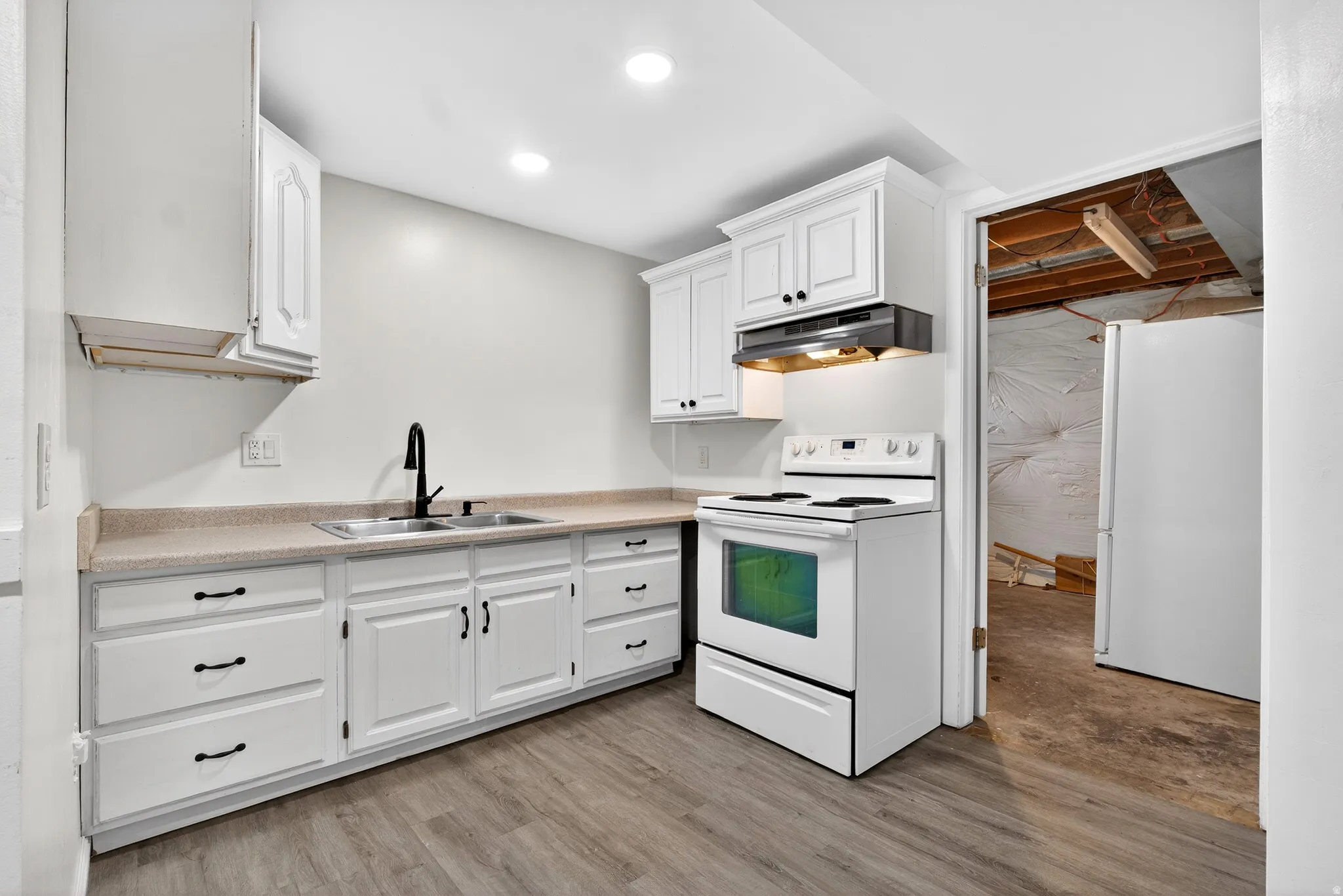 Kitchen with white appliances, white cabinetry, light countertops, and light wood-style flooring