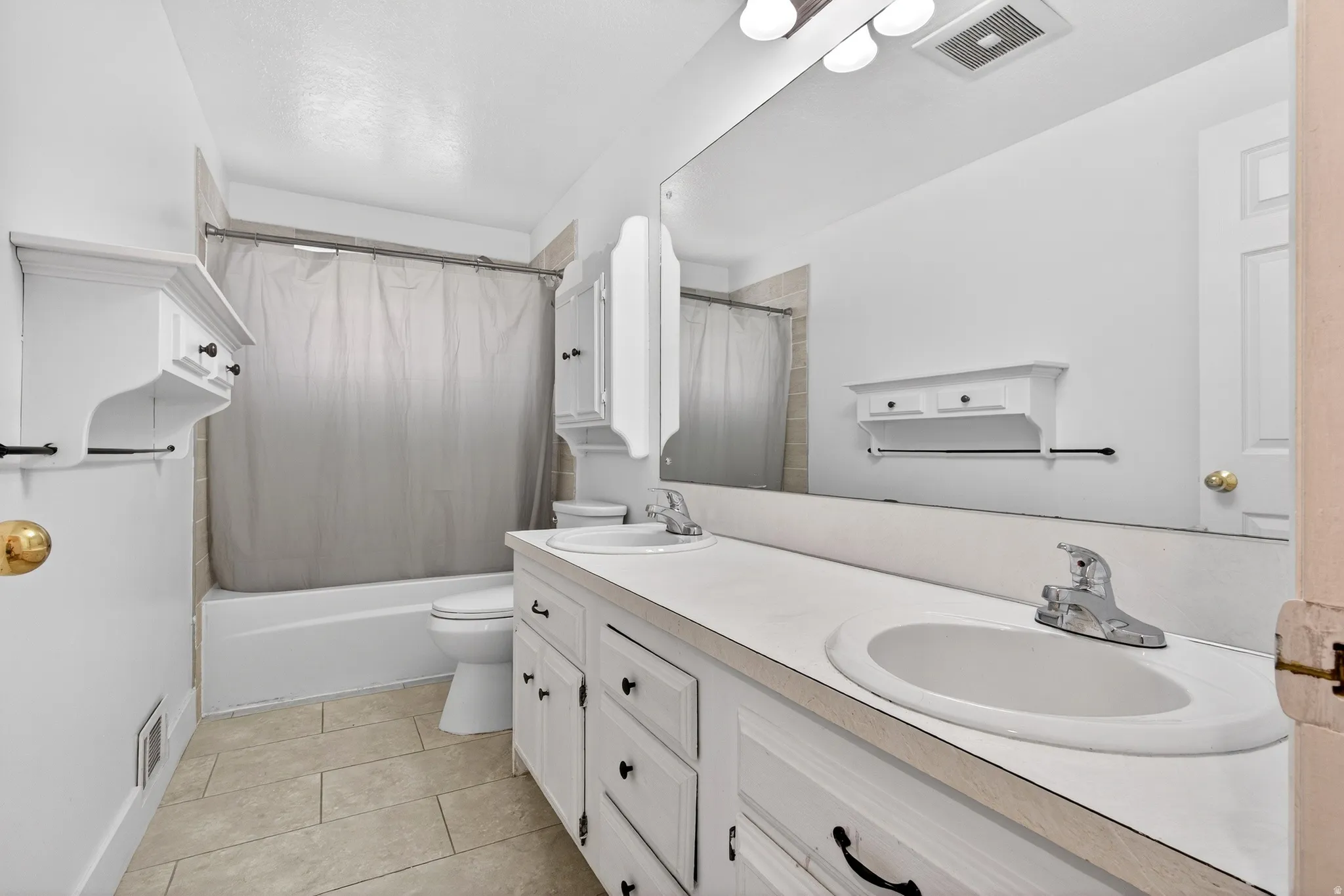 Bathroom with double vanity, shower / tub combo, and light tile patterned flooring
