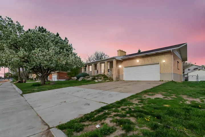 Single story home featuring brick siding, concrete driveway, an attached garage, a chimney, and a yard
