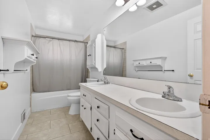 Bathroom with double vanity, shower / tub combo, and light tile patterned flooring