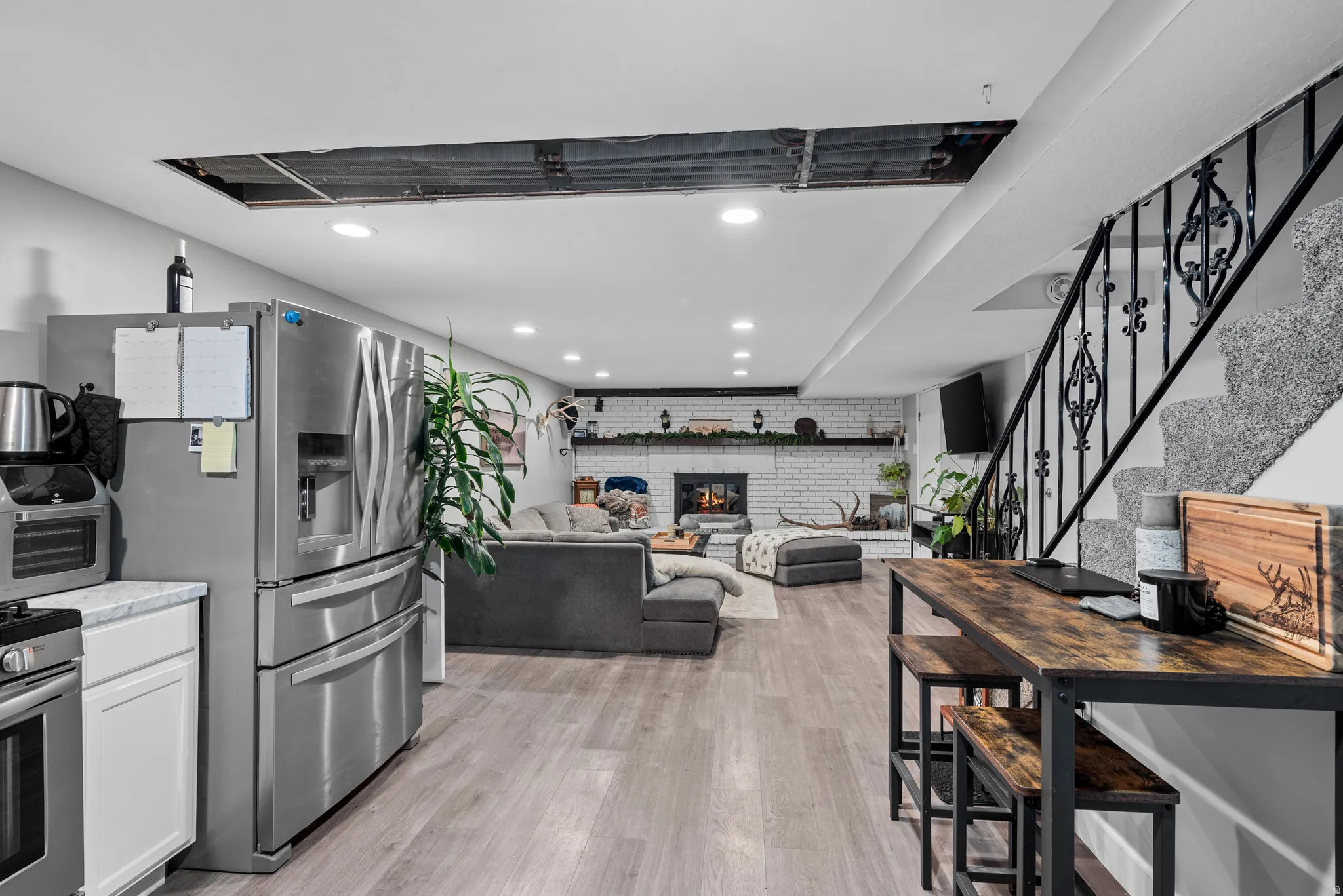 Kitchen featuring stainless steel fridge, brick wall, recessed lighting, light wood finished floors, and a brick fireplace