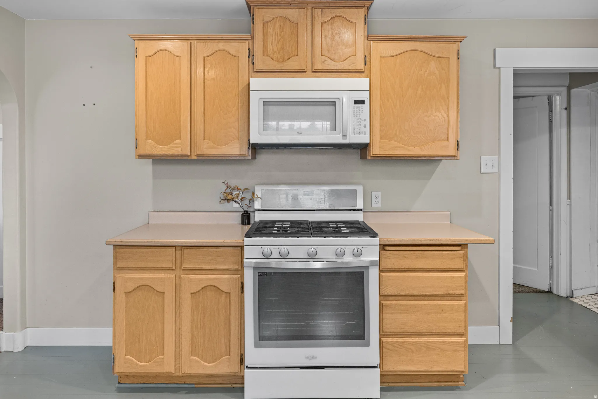 Kitchen with gas range, light countertops, white microwave, and light wood finish cabinetry