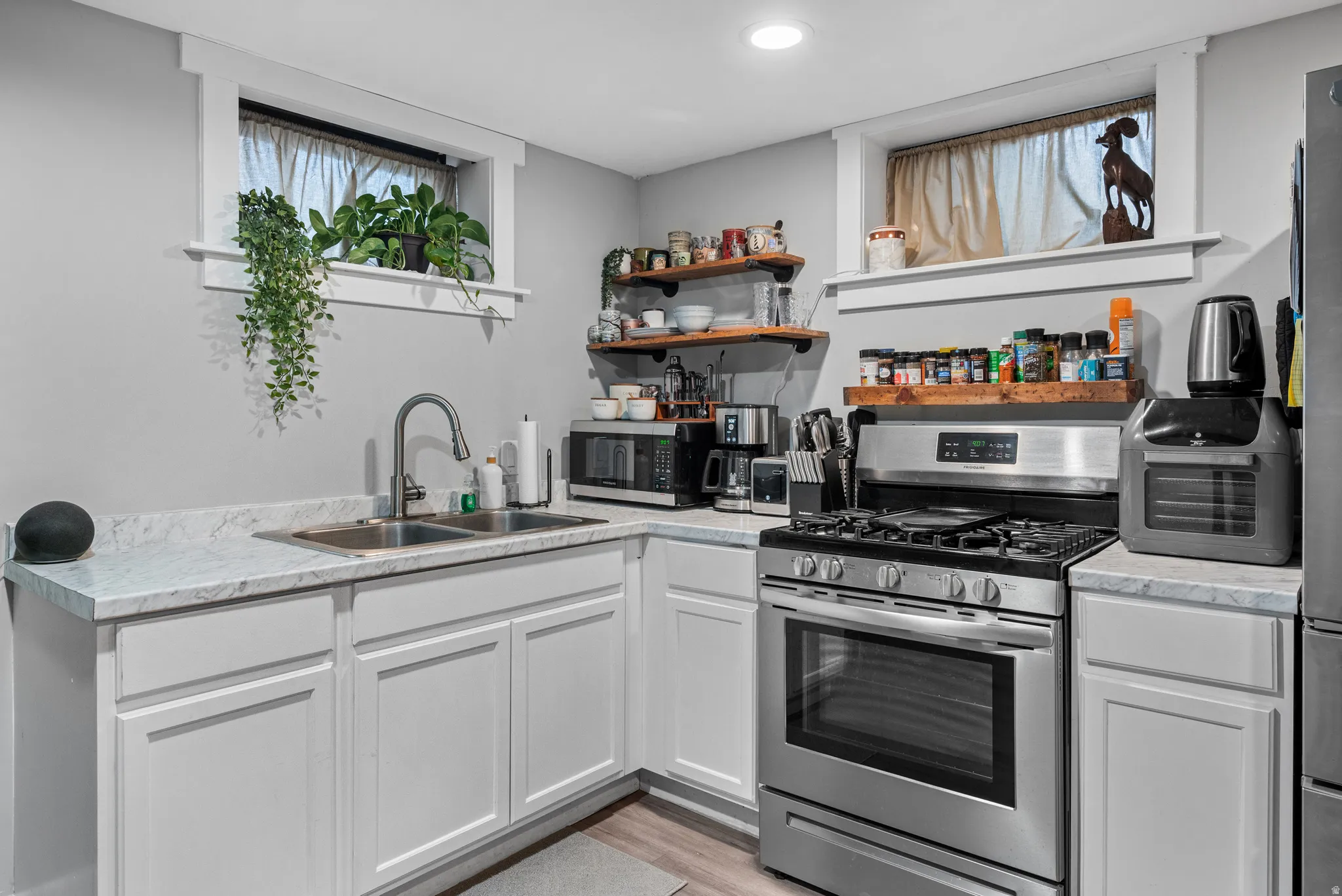 Kitchen with stainless steel appliances, light countertops, white cabinetry, light wood-style floors, and open shelves