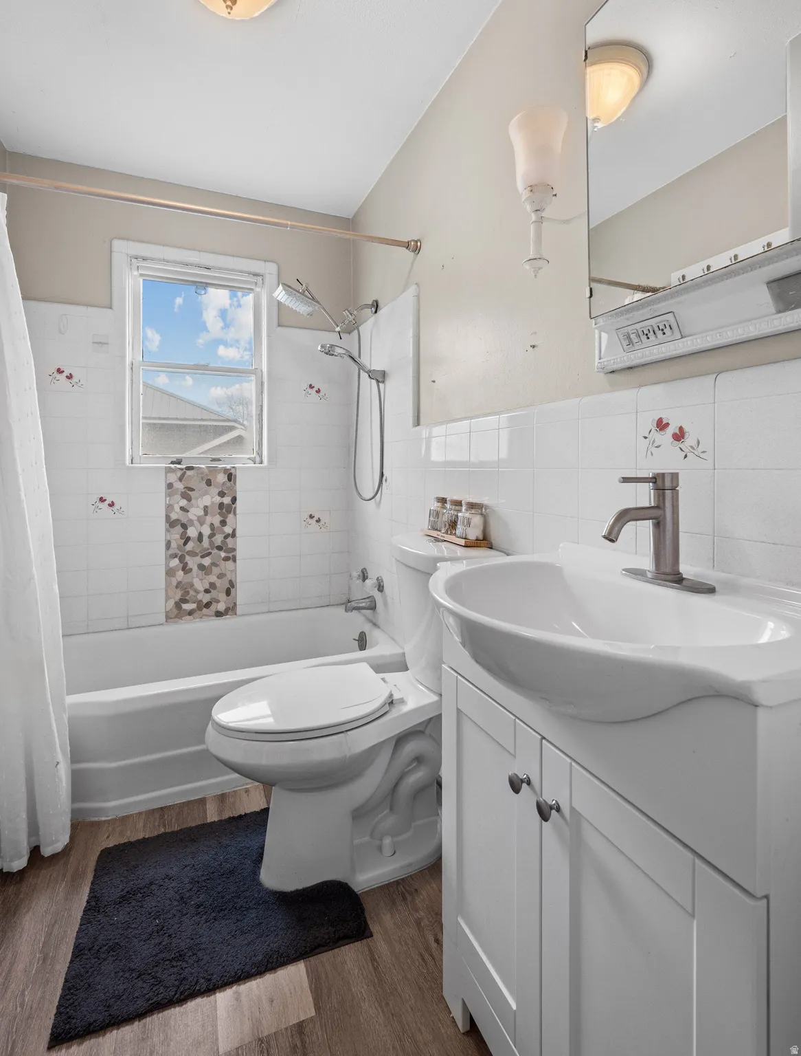 Bathroom with vanity, tile walls, dark wood-style flooring, shower / bathtub combination with curtain, and wainscoting