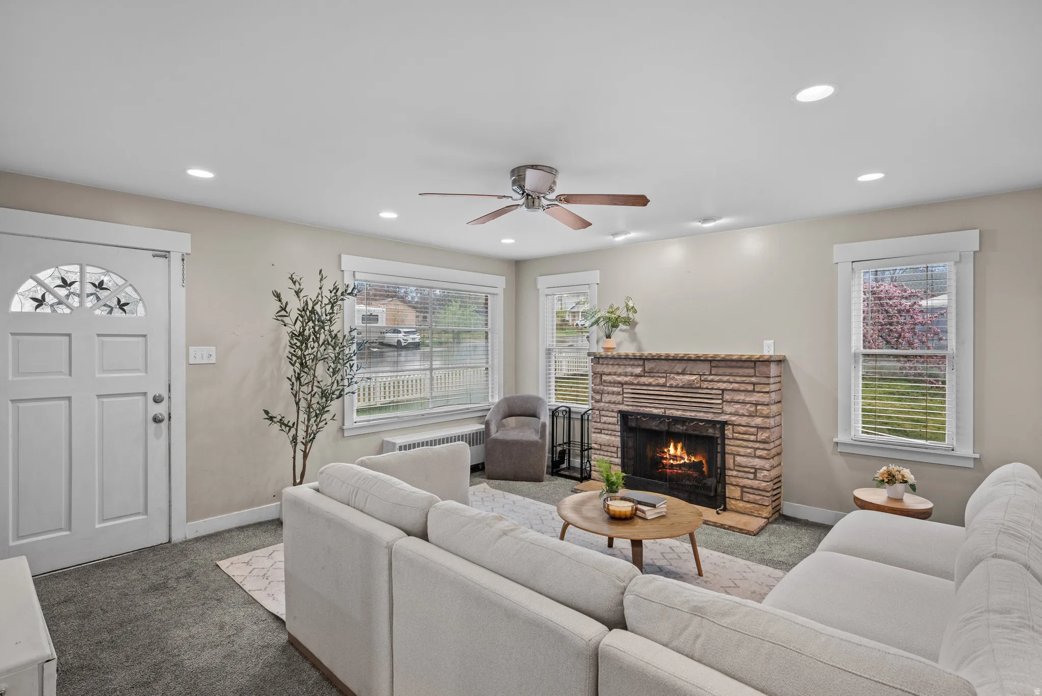 Living room with a fireplace, carpet floors, ceiling fan, radiator, and recessed lighting