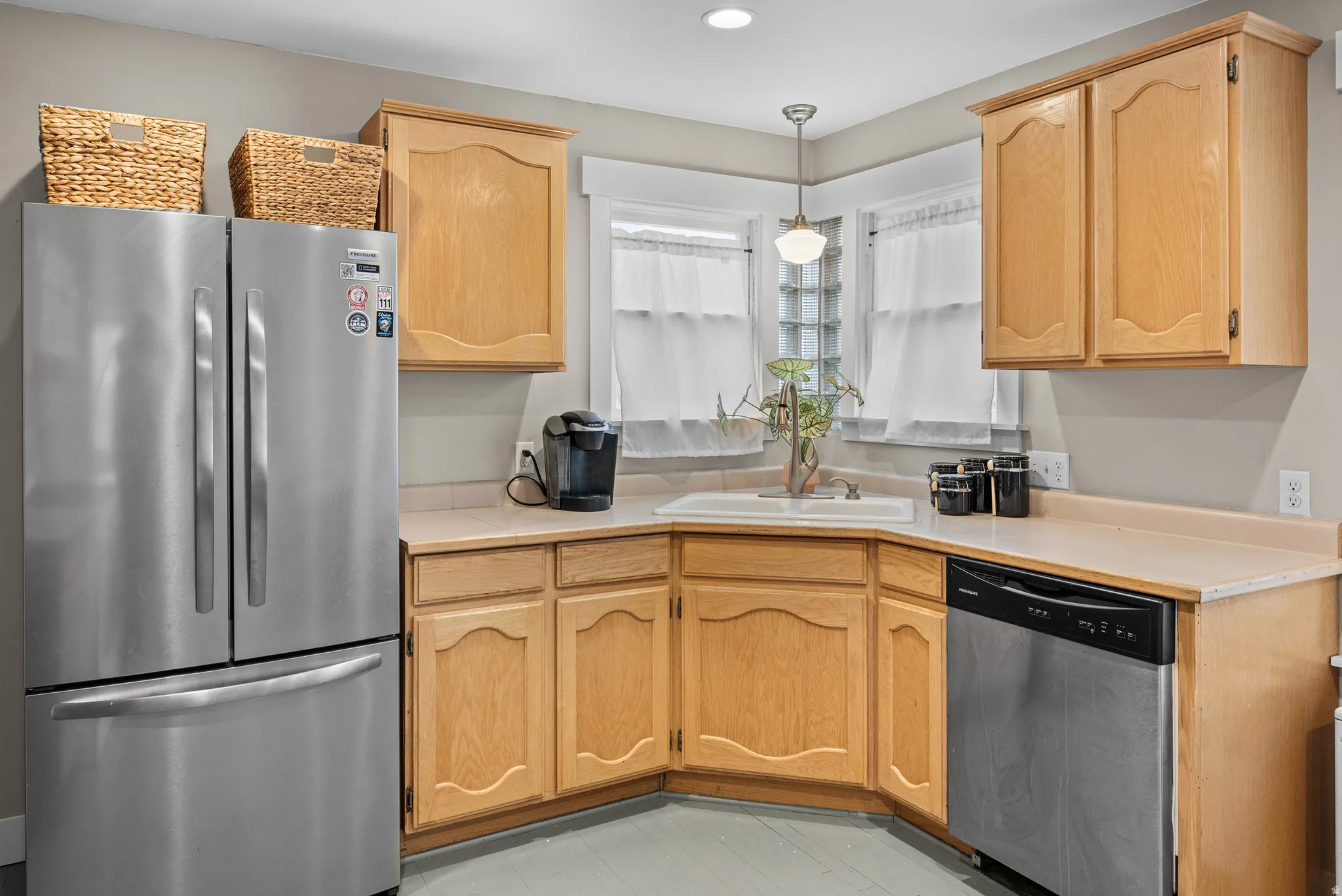 Kitchen with stainless steel appliances, light countertops, pendant lighting, and light wood finish cabinets