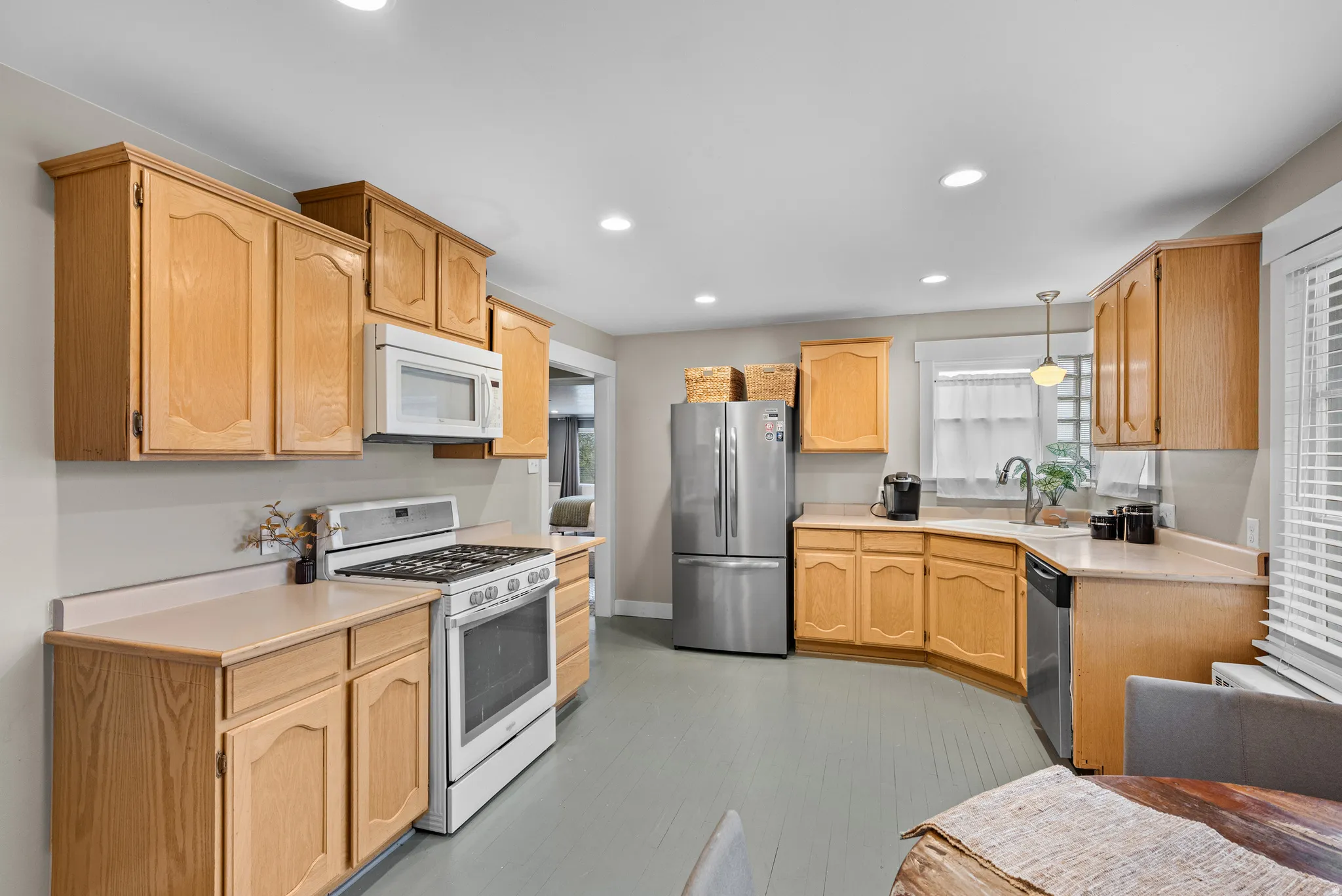 Kitchen with light countertops, stainless steel appliances, light wood finish cabinets, and decorative light fixtures