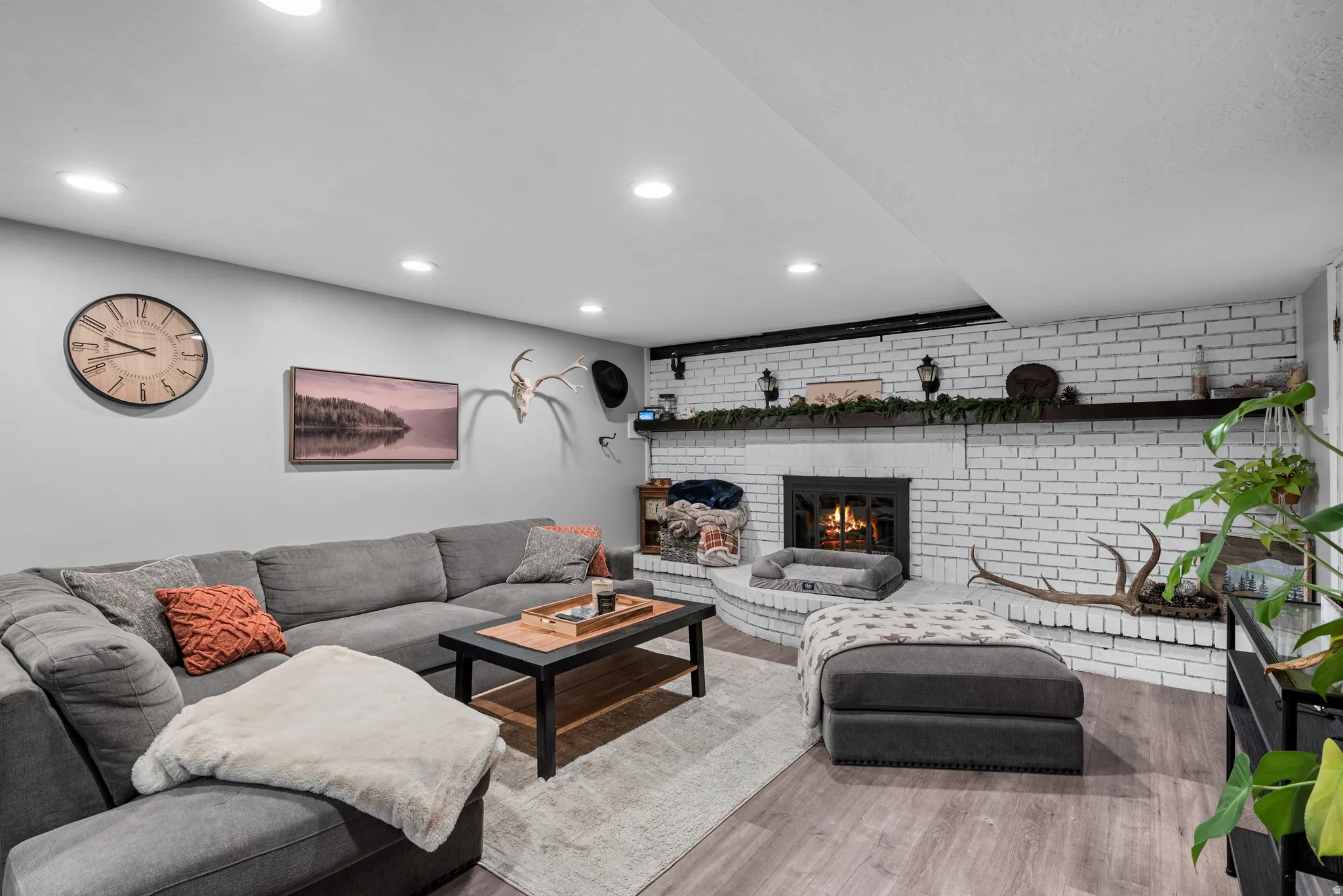 Living area with brick wall, wood finished floors, a fireplace, recessed lighting, and an accent wall