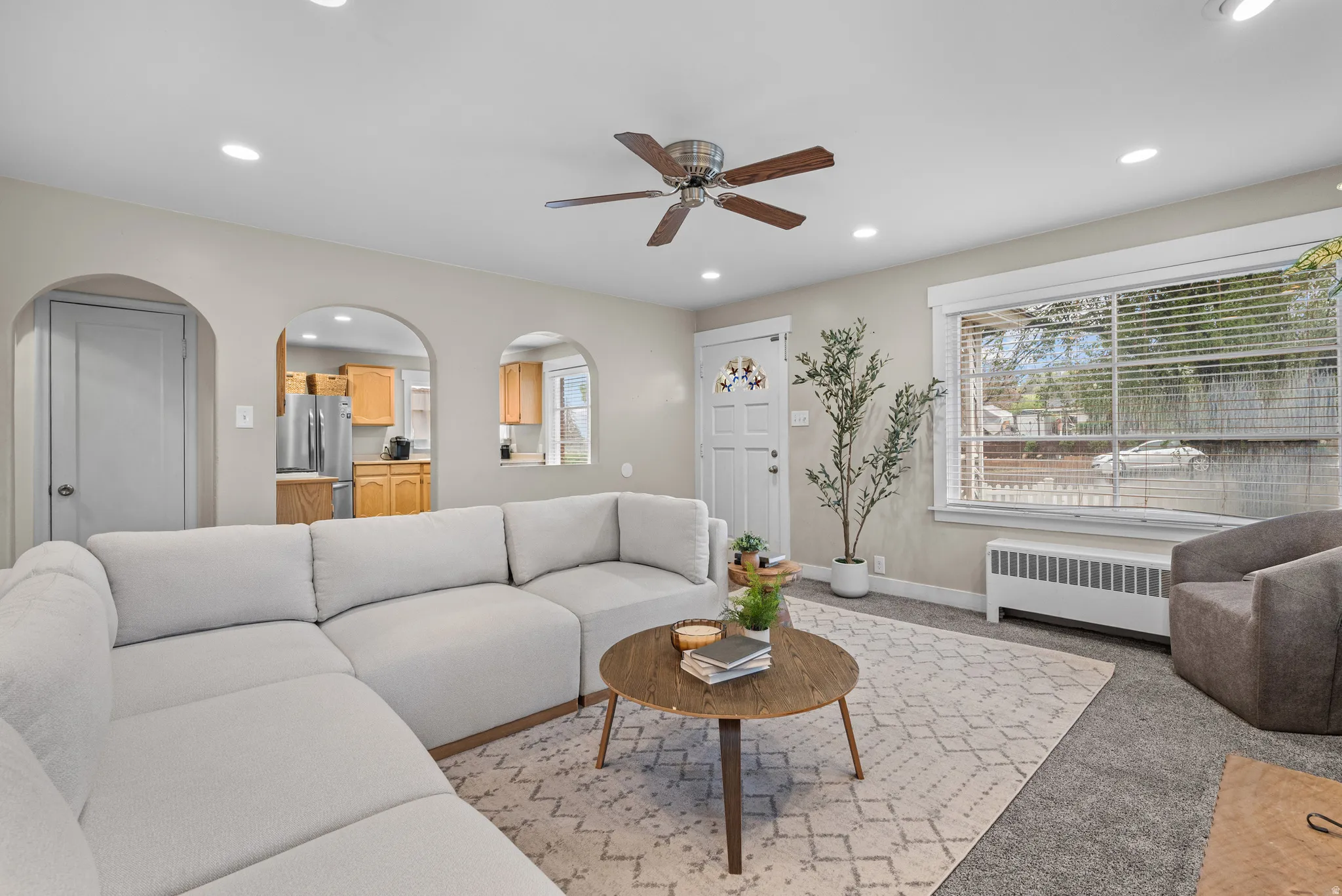 Living room with radiator, a ceiling fan, recessed lighting, light colored carpet, and arched walkways